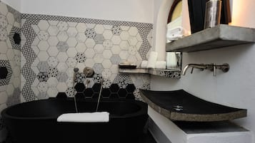 A modern bathroom with a black freestanding bathtub, a stone sink, and a tiled wall with geometric patterns.