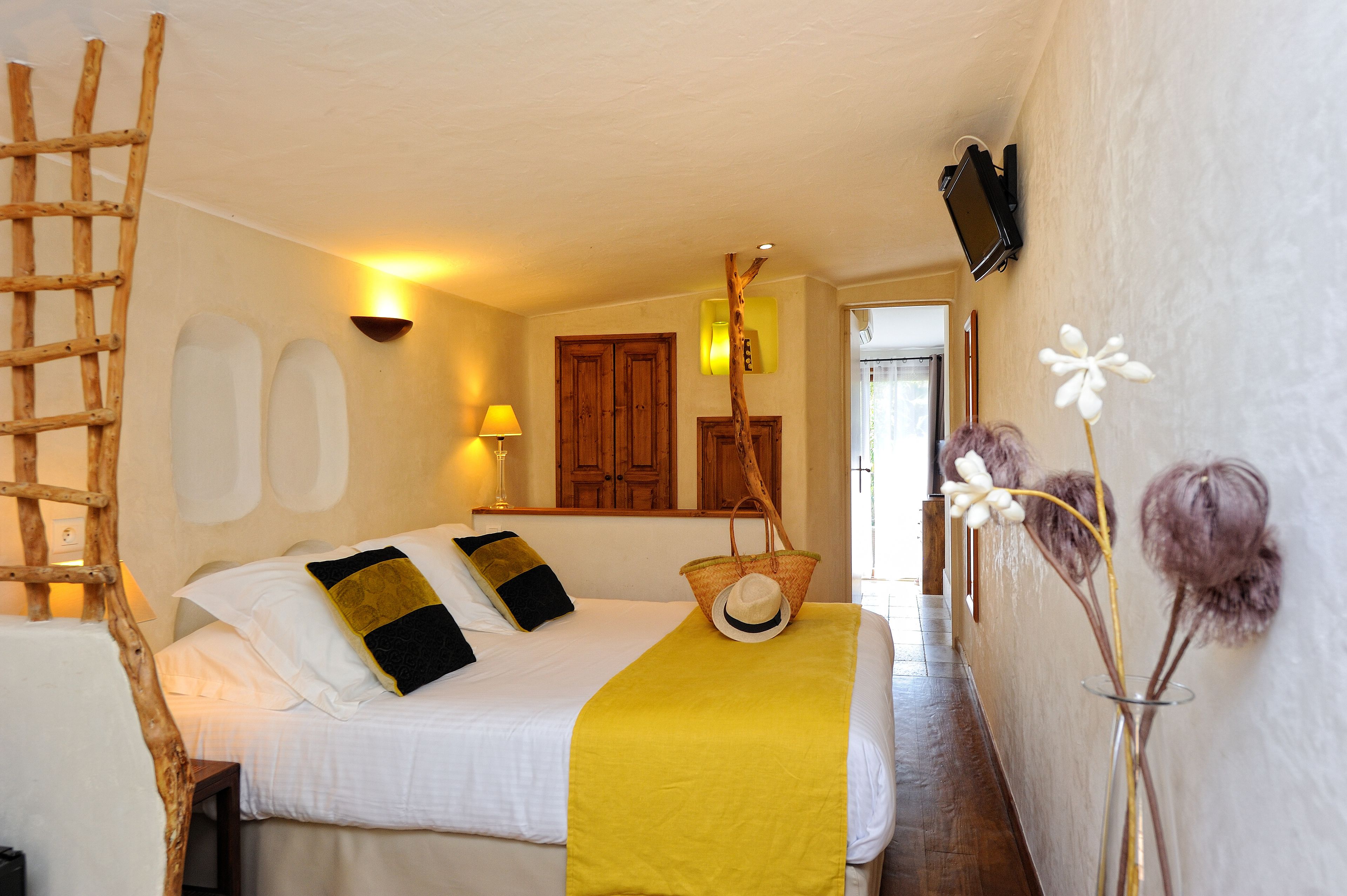 Un dormitorio con una cama, una escalera de madera, una cesta y un florero con flores.