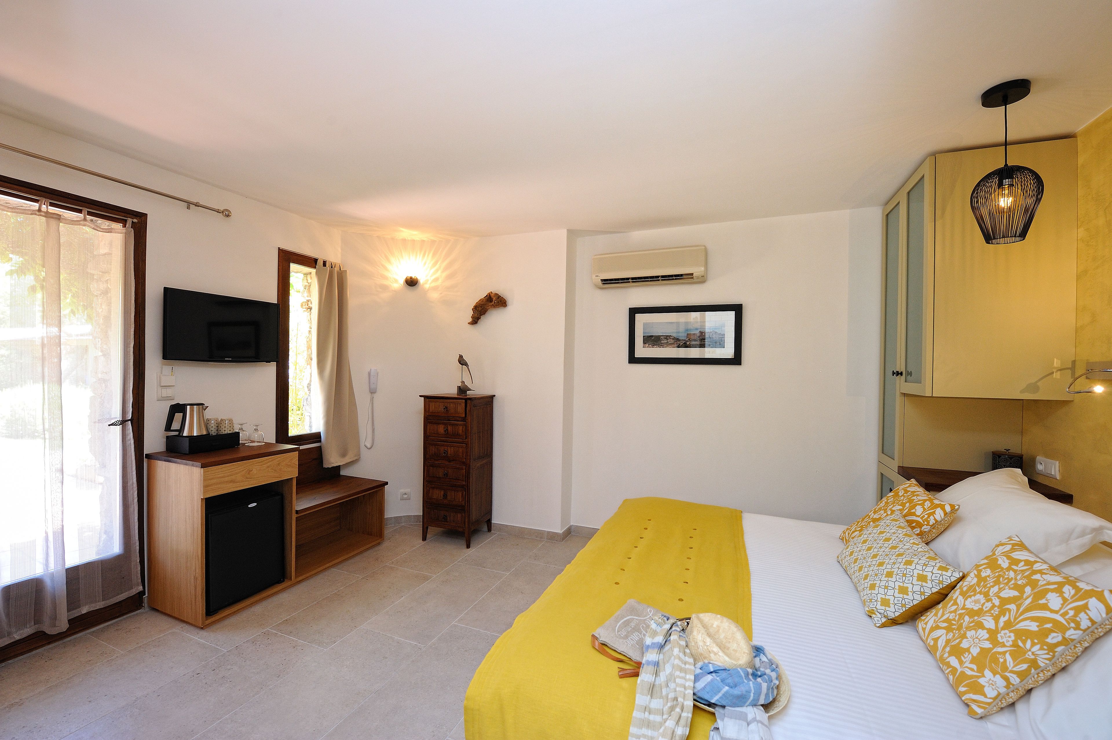 A hotel room with a bed, a desk with a TV, an air conditioner, and a window with curtains.