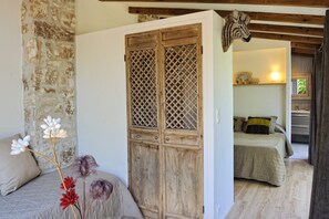 Un dormitorio rústico con un armario de madera, una cama con edredón color beige y una pared de piedra.
