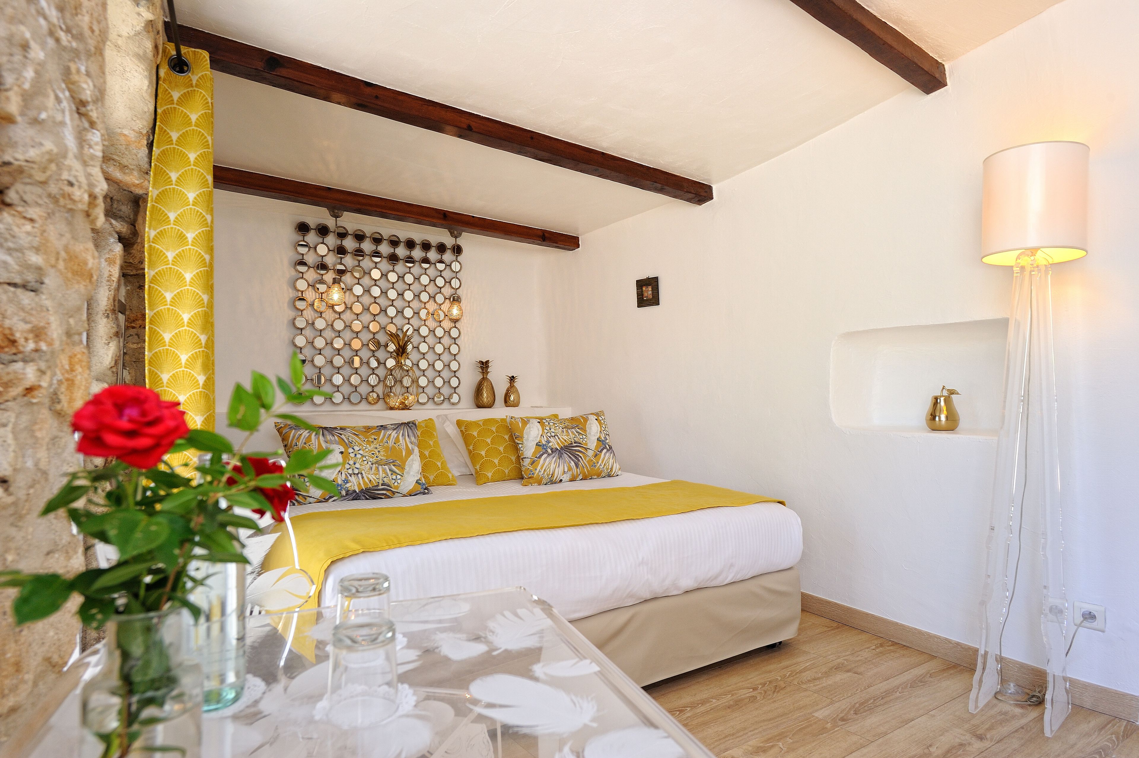 A bedroom with a bed, a bedside table, a vase with a red rose, a wall-mounted light fixture, and a decorative wall panel.