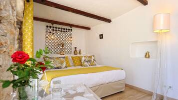 A bedroom with a bed, a bedside table, a vase with a red rose, a wall-mounted light fixture, and a decorative wall panel.
