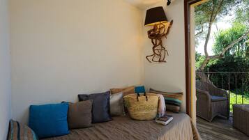 Une chambre à coucher avec un lit, des oreillers, une lampe et une chaise en osier sur un balcon.