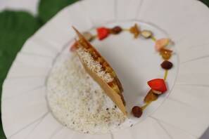 Un postre sobre un plato blanco con un diseño original, que incluye una pieza con forma de cono, una base cremosa y adornos coloridos.