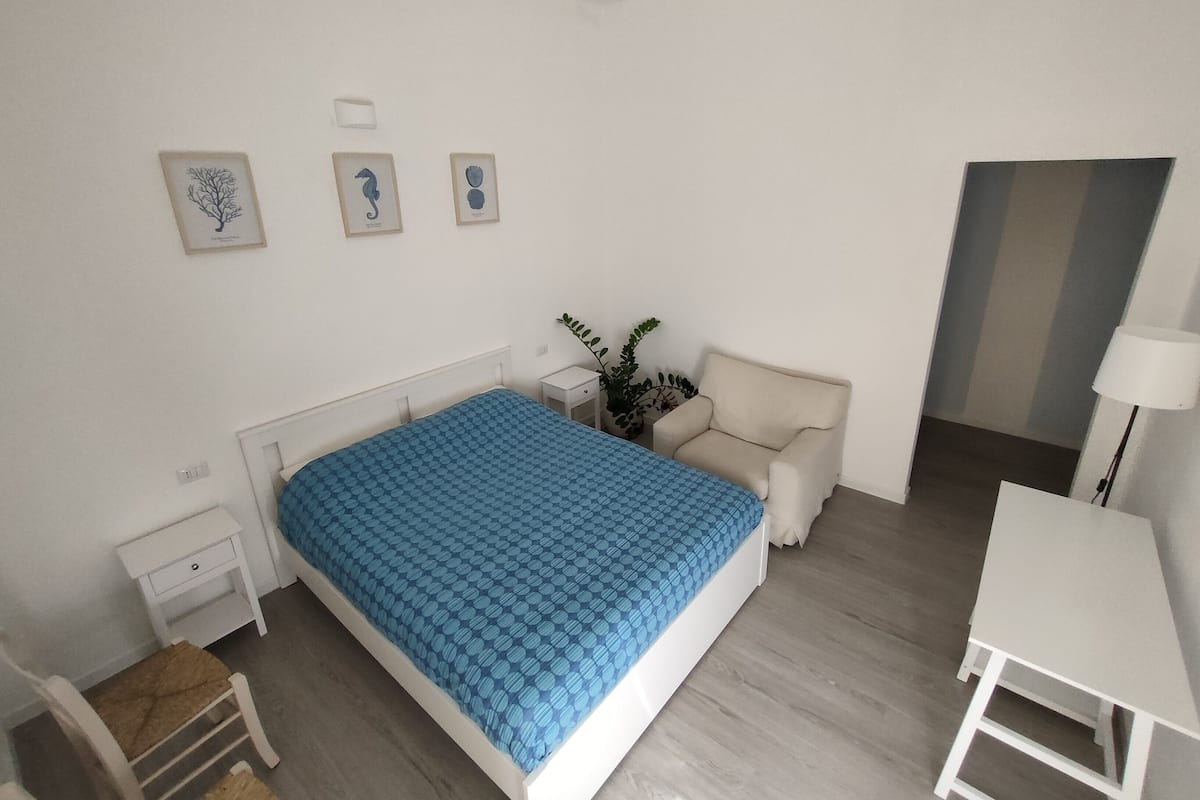 A bedroom with a bed, a chair, a desk, and a nightstand.