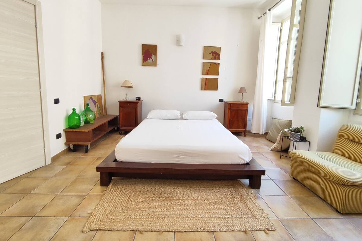 A bedroom with a large bed, two bedside tables, a small cabinet, and a sofa.