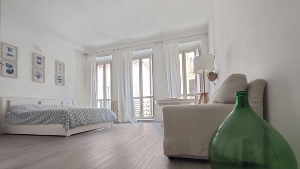 A bedroom with a bed, a chair, a green vase, and a window with curtains. - Casa Marina (Cagliari)