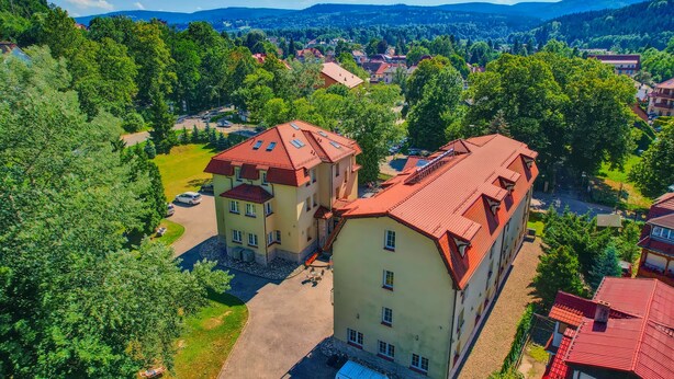 Ett flygbildsbild av ett bostadsområde med flera byggnader, inklusive ett framträdande tvåvåningshus med ett rött tak och en mindre sammanbyggd del.