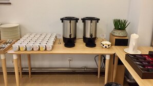 En kaffestation med två kaffedispensrar, ett urval av olika typer av muggar och en liten skylt med texten ”Koda Coffee”.