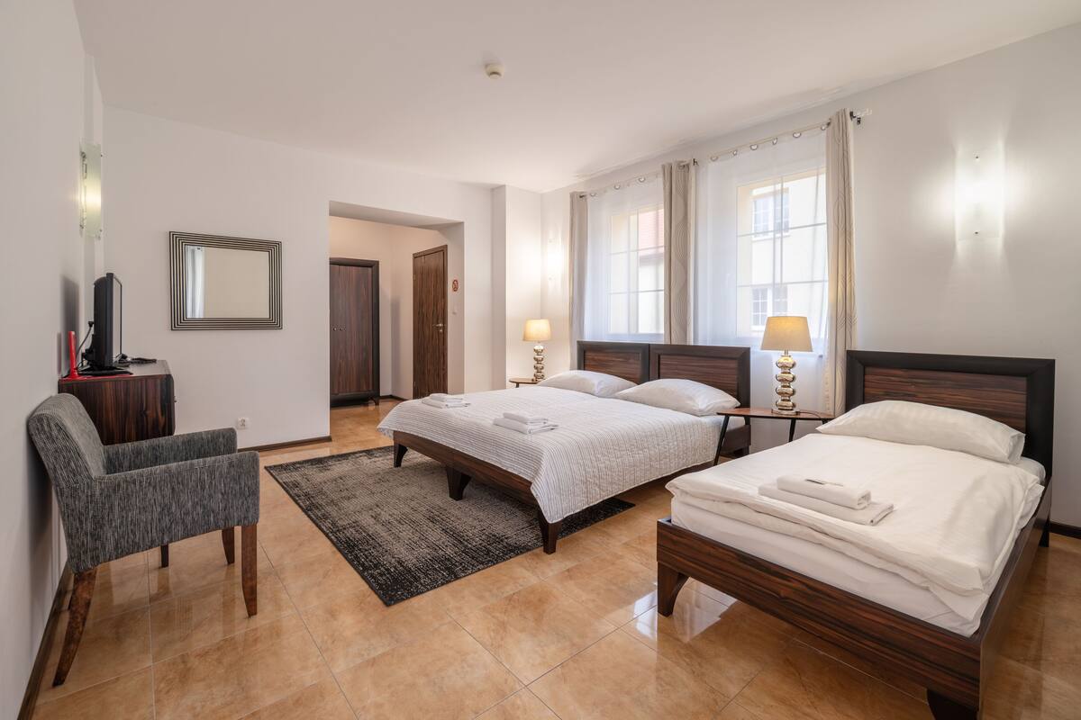 A hotel room with two beds, a desk, a chair, a TV, and a window with curtains.