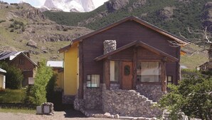 Una casa de madera rústica con base de piedra, frente a un paisaje montañoso.