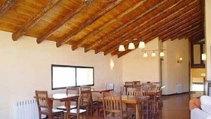 Un comedor amplio con mesas y sillas de madera, un alto techo de madera y un gran ventanal que proporciona luz natural.
