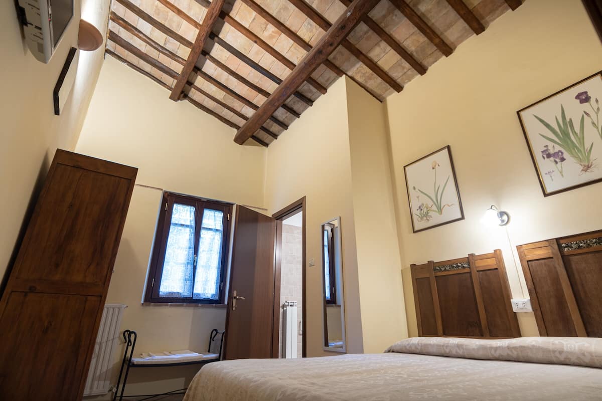 A bedroom with a wooden ceiling, a bed, a window, a radiator, and a mirror.