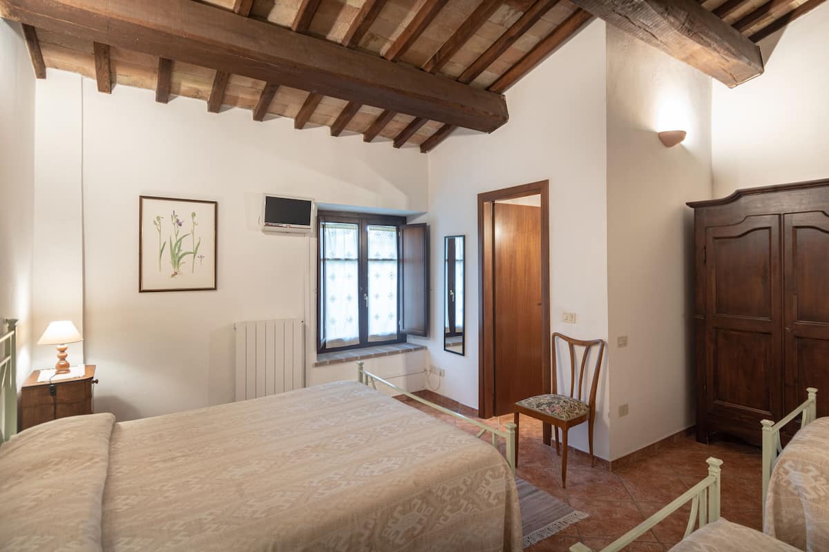 A bedroom with a wooden ceiling, a bed, a chair, a wardrobe, and a window with curtains.