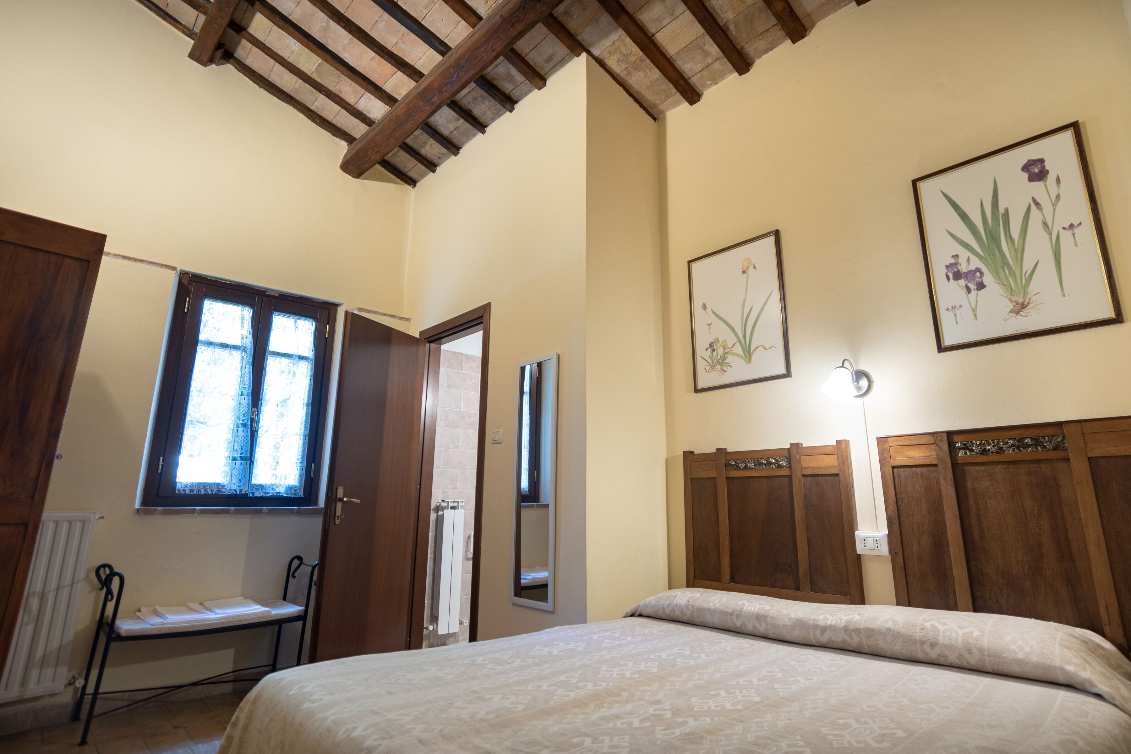 A bedroom with a bed, wooden headboard, a window, and two framed botanical prints on the wall.