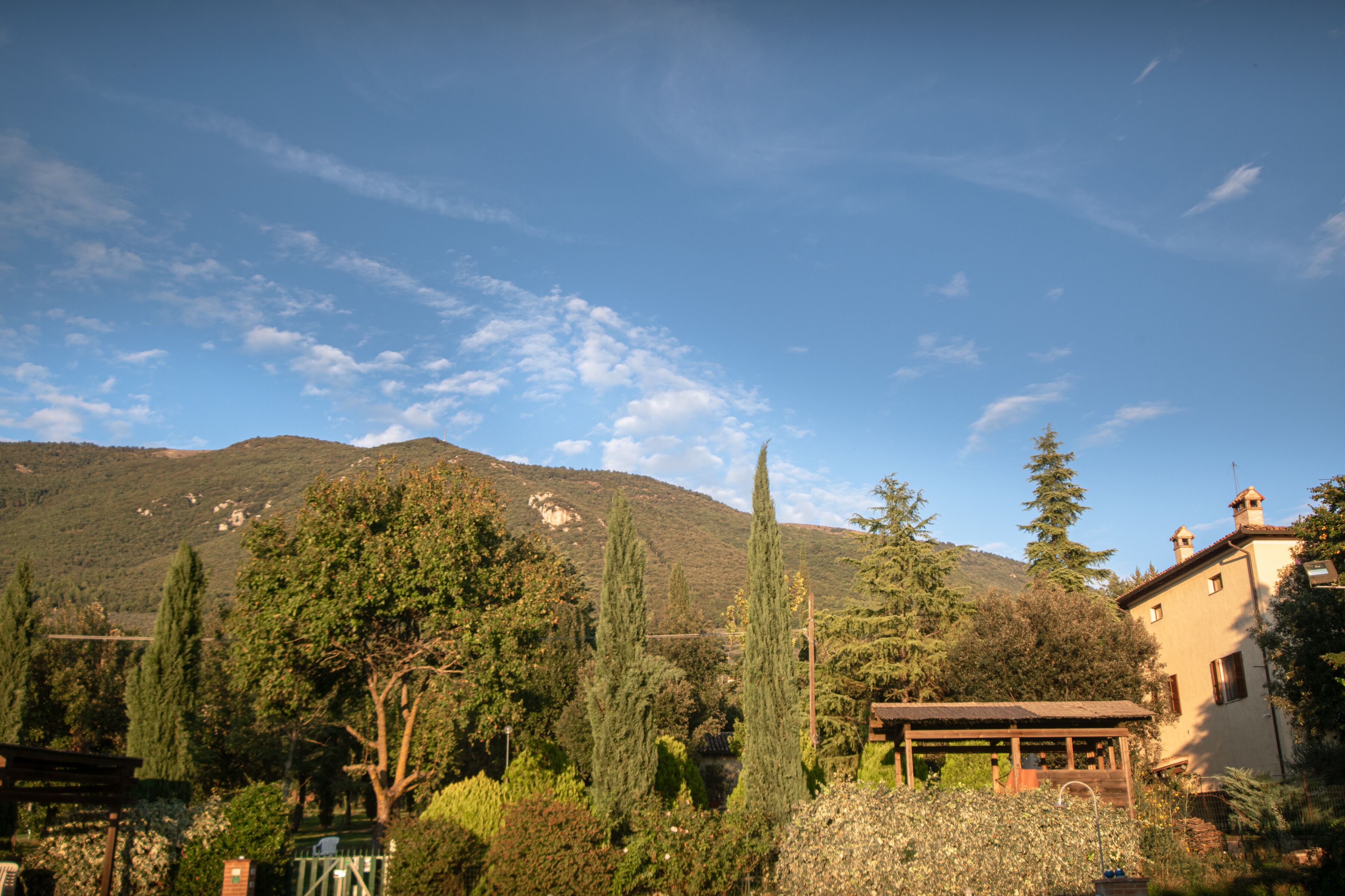 A rural landscape with a mountain in the background, a wooden gazebo, and a building with a sloped roof.