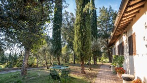 A pathway leading to a building with a white exterior and wooden shutters. There are trees and a bench along the path. - Agriturismo Sasso Rosso (Assisi)