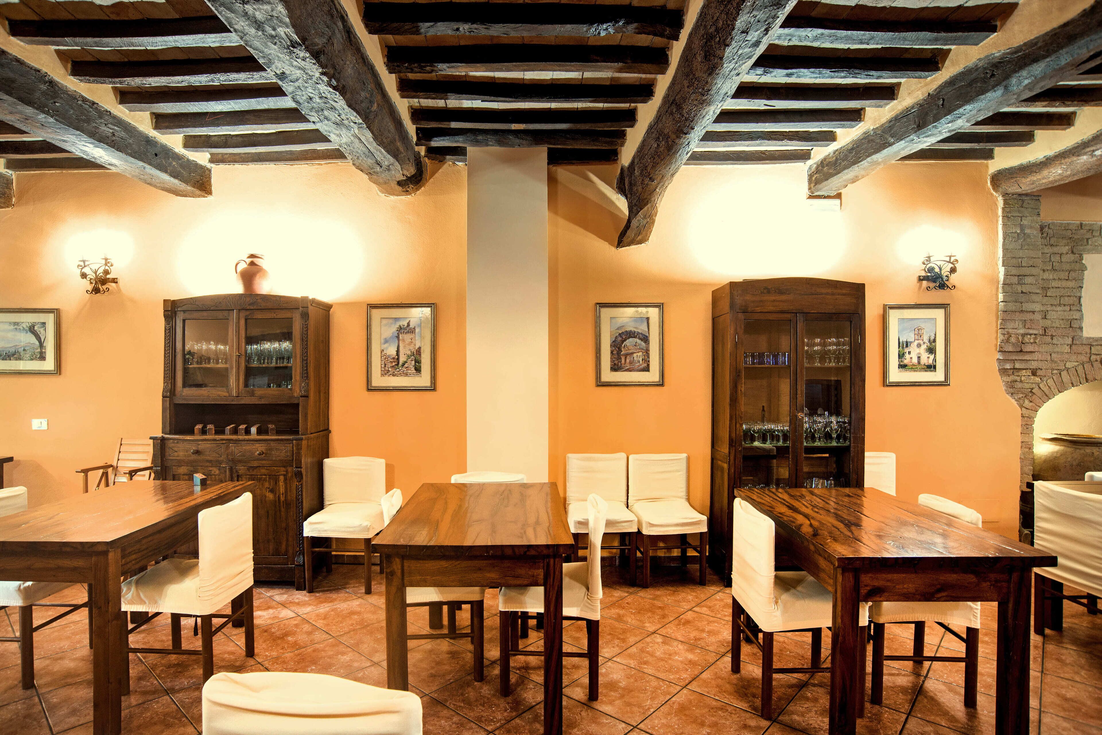 A dining area with wooden tables and chairs, a cabinet with glassware, and framed pictures on the walls.