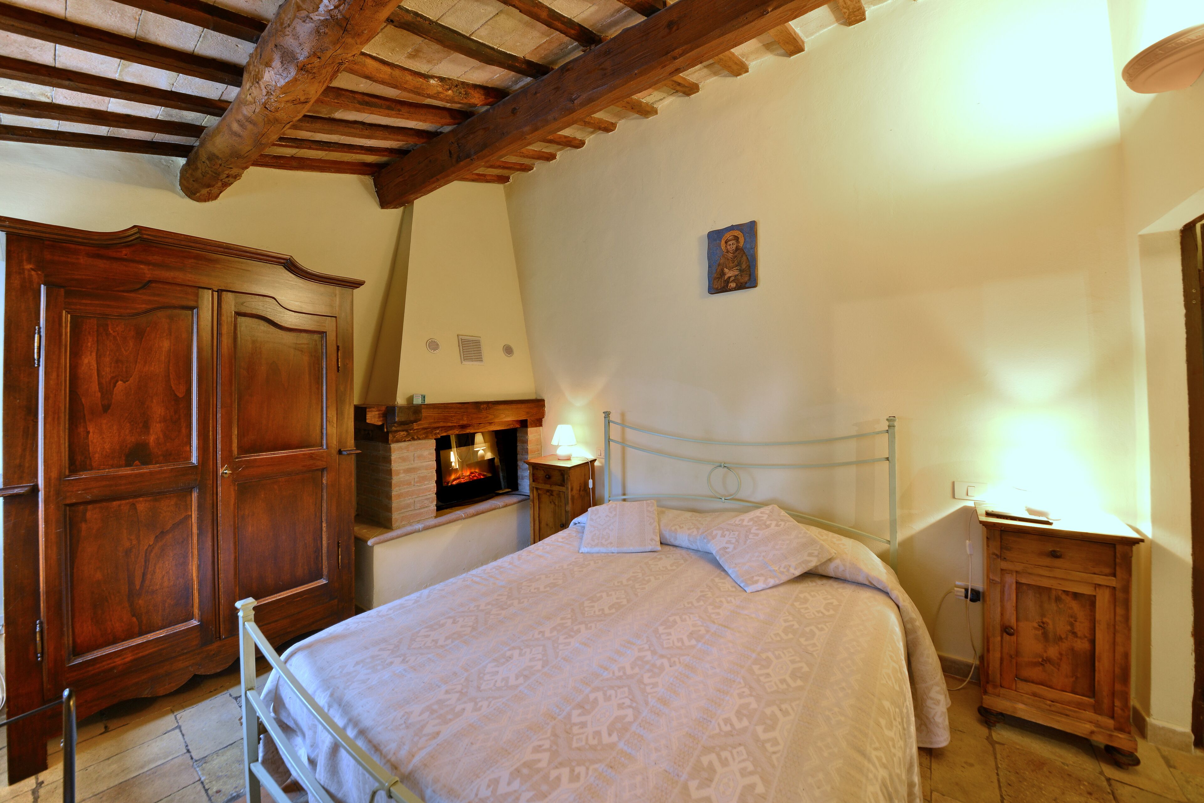 A bedroom with a bed, wooden wardrobe, and a small bedside table with a lamp.