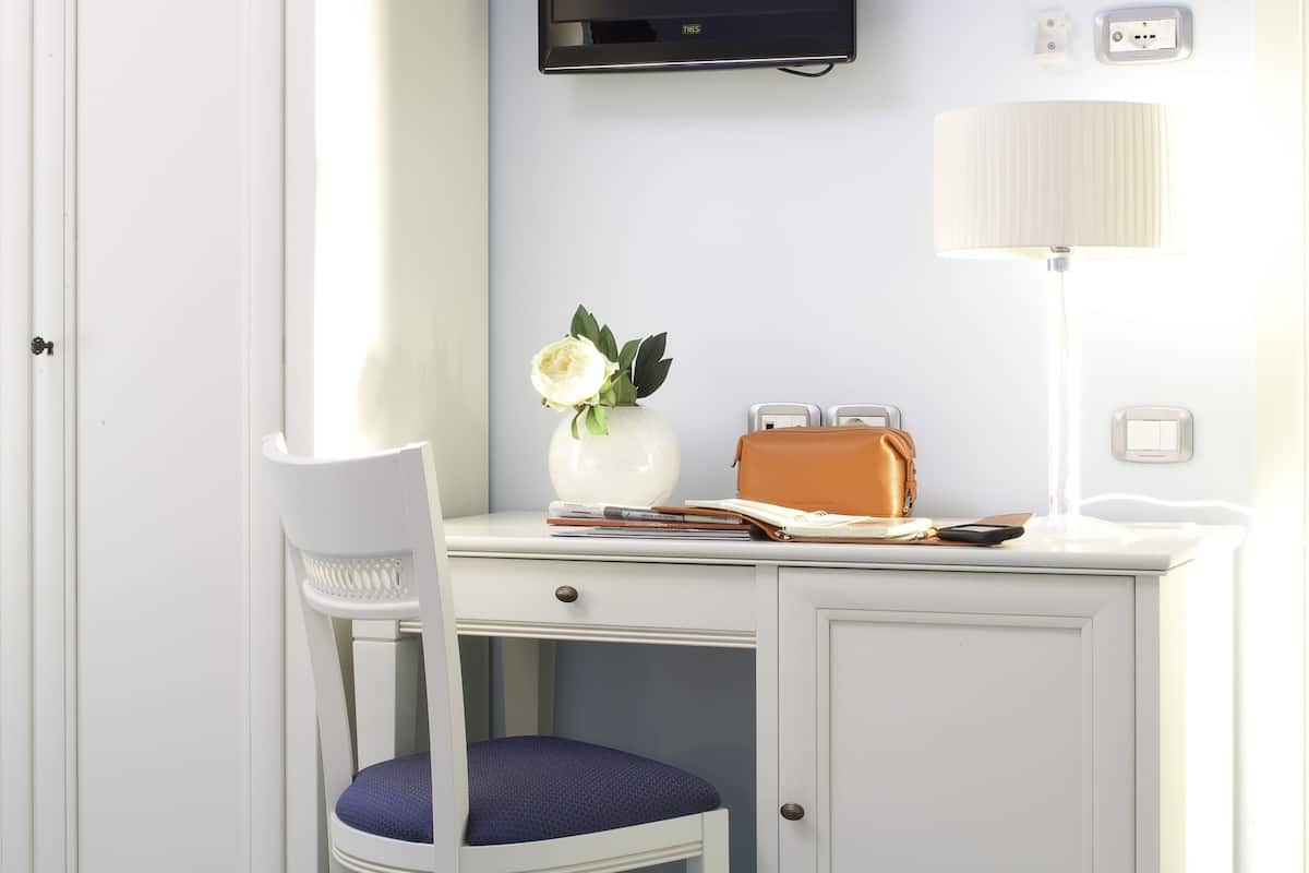 A room with a white desk, a chair, a bed, and a television mounted on the wall.