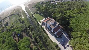 Vista aérea de una propiedad costera con un edificio principal, un estacionamiento y una playa.