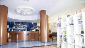 A hotel lobby with a reception desk, bar area, and a bookshelf filled with magazines. - Hotel Parco dei Principi (Capaccio-Paestum)