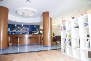 Um hall de hotel com balcão de recepção, área de bar e uma estante cheia de revistas.