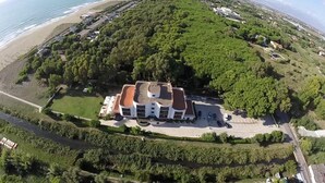 An aerial view of a large, multi-story building surrounded by lush greenery, with a beach and ocean in the background. - Hotel Parco dei Principi (Capaccio-Paestum)