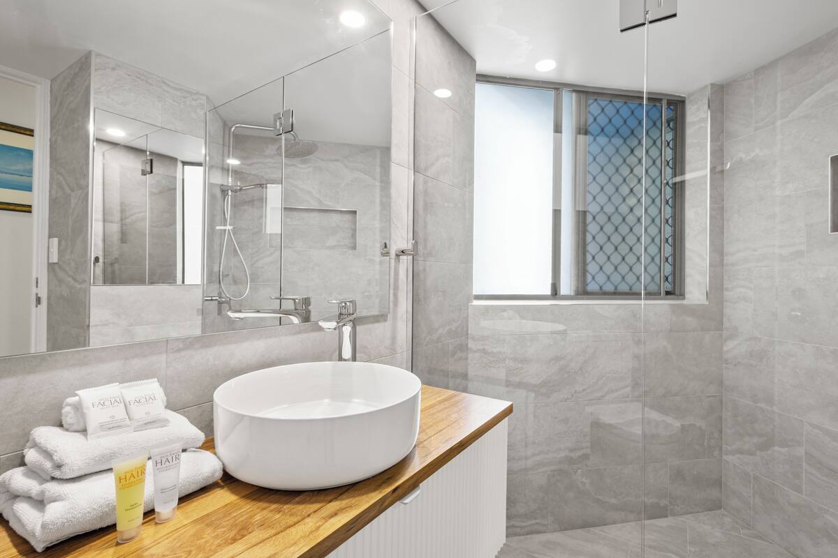 A modern bathroom with a large mirror, a round white sink, and a glass-enclosed shower.