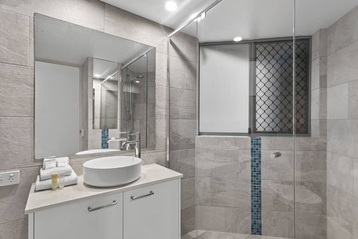 A modern bathroom with a large mirror, a round sink, and a glass-enclosed shower area.