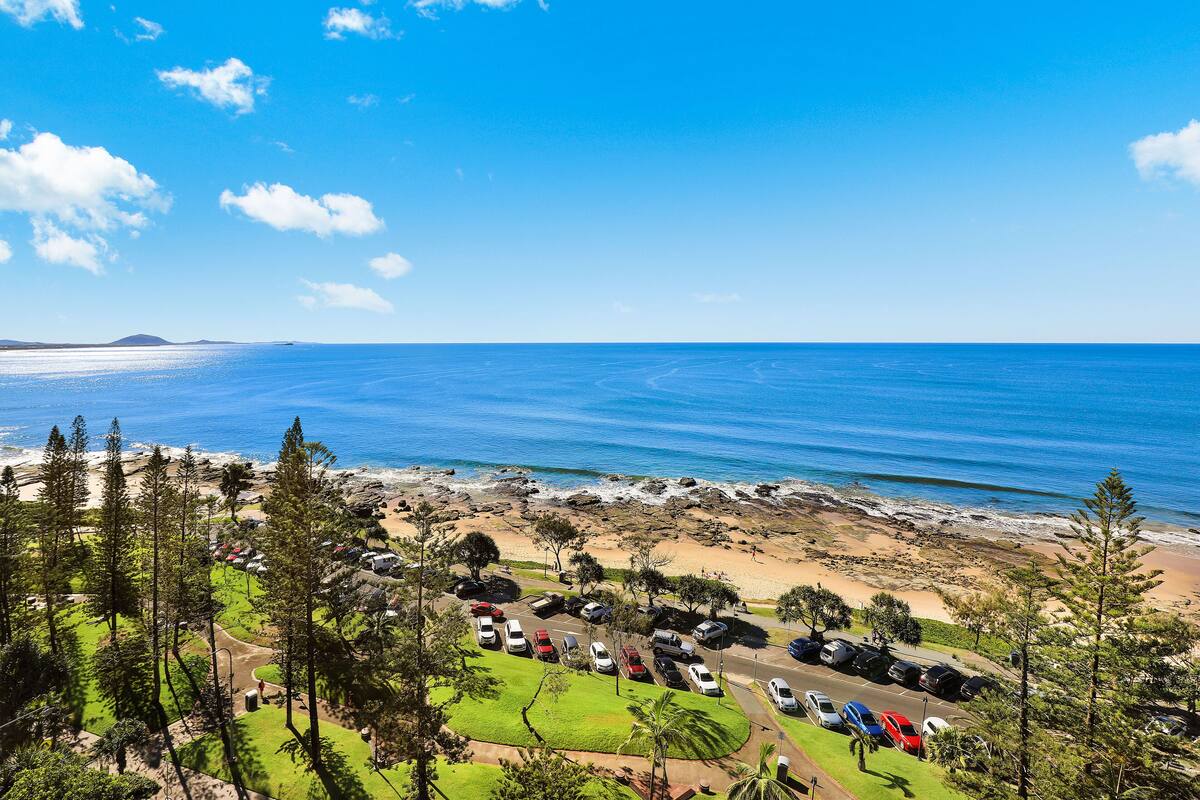 A coastal view with a parking area, beach, and ocean.