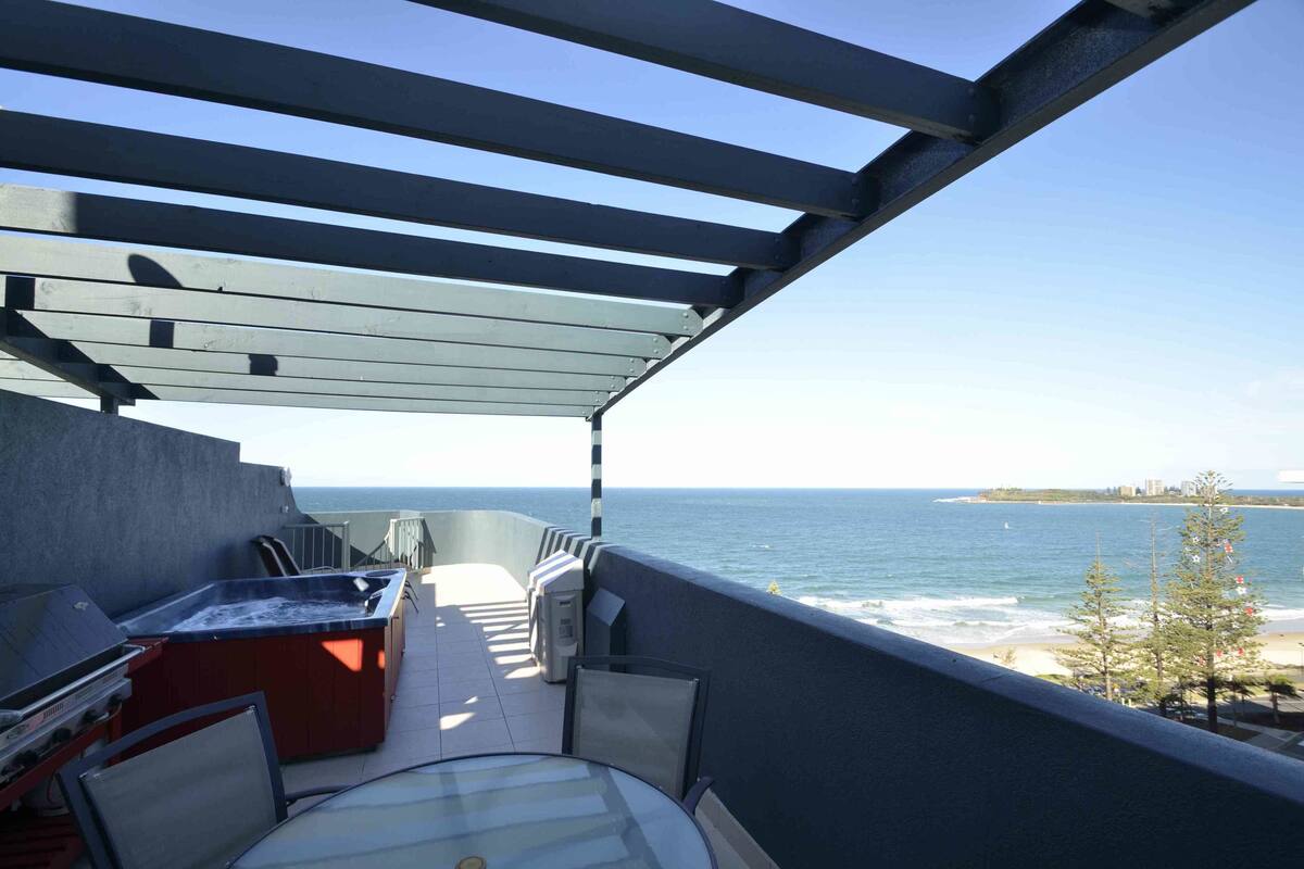 A balcony with a hot tub, seating, and a view of the ocean.
