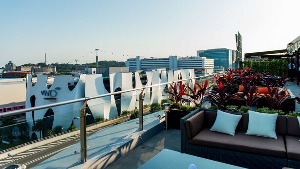 A rooftop terrace with a modern lounge area, a view of the city skyline, and a distinctive architectural structure in the background. - Travelodge Harbourfront (Singapore)