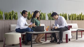 Tres personas sentadas en una mesa con portátiles, en un entorno exterior moderno con pared de madera y plantas verdes.