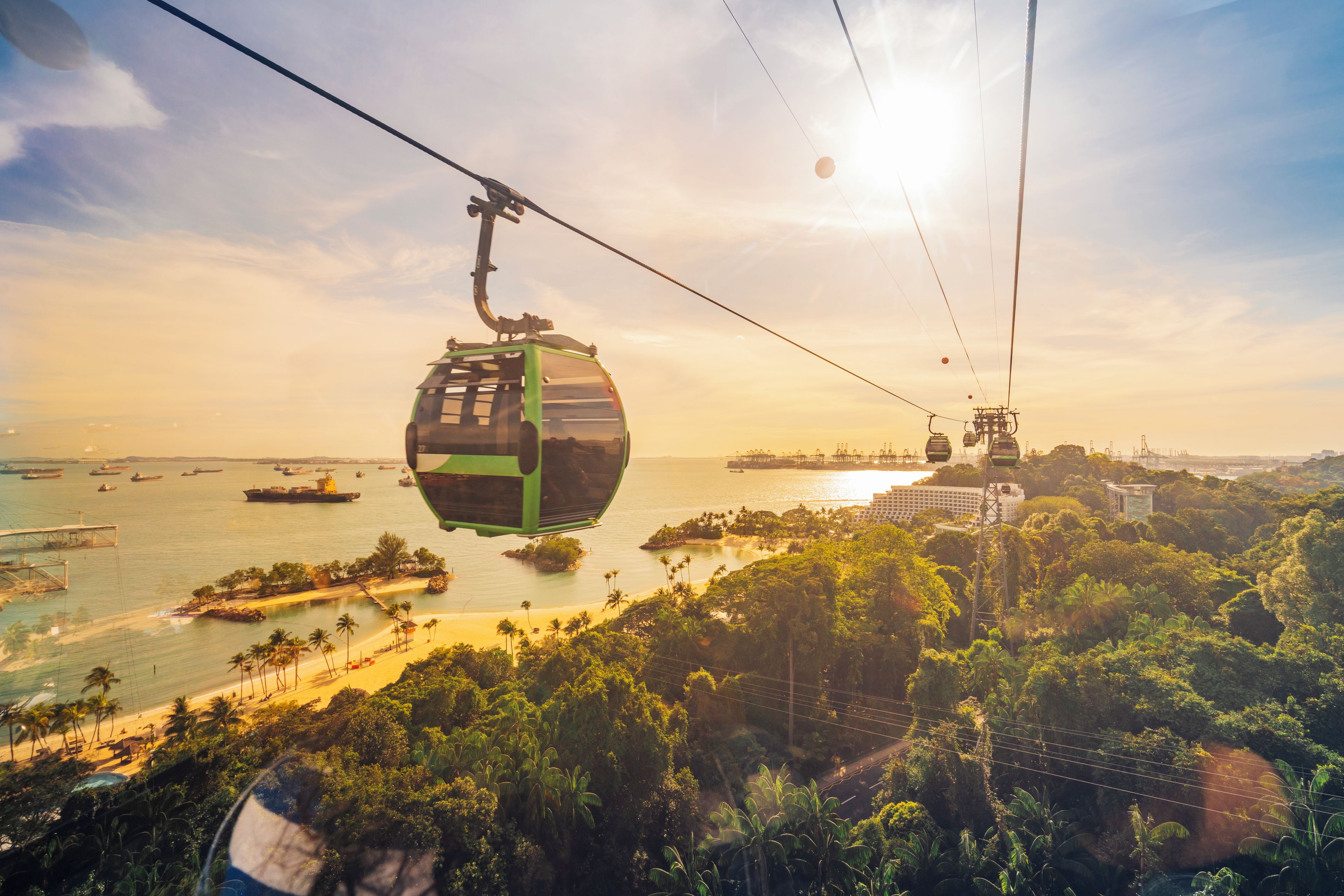 A cable car system with a view of a coastal area including a beach and ships in the distance.