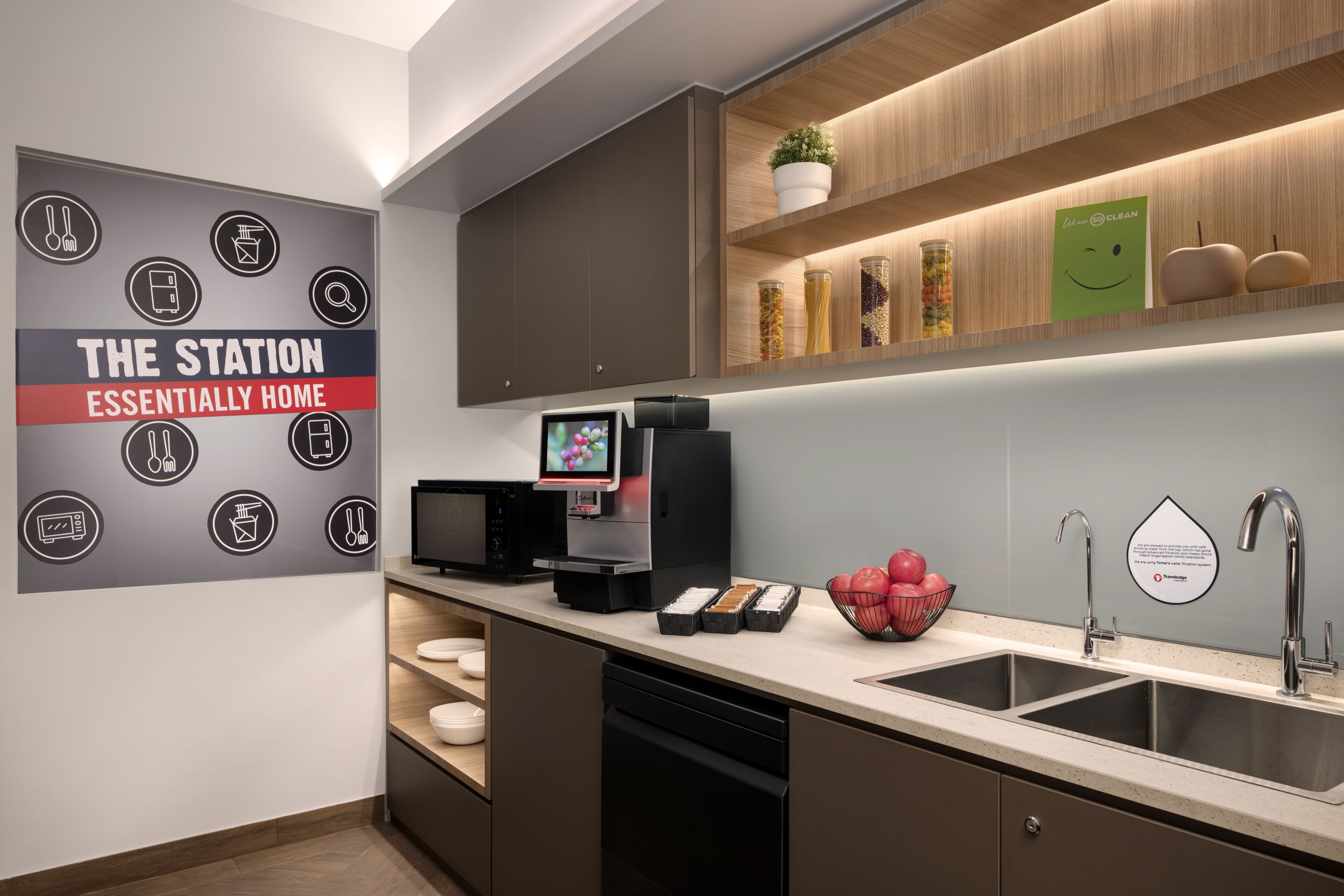 A modern kitchen with a built-in microwave, a coffee machine, and a sink. There is a wall-mounted shelf with jars and a potted plant.