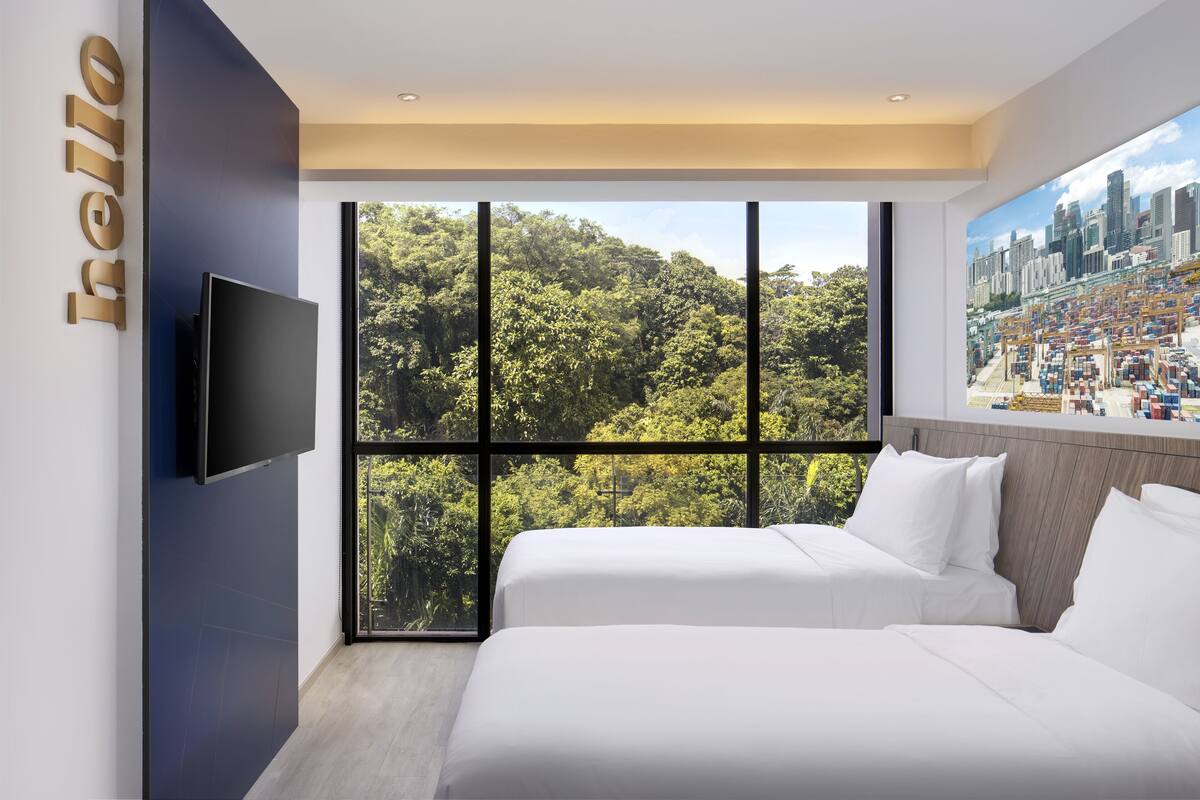 Ein modernes Hotelzimmer mit großem Fenster, das Blick auf einen Wald und eine Stadt bietet.