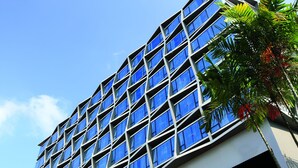 A modern building with a grid of windows and a palm tree in the foreground. - Travelodge Harbourfront (Singapore)