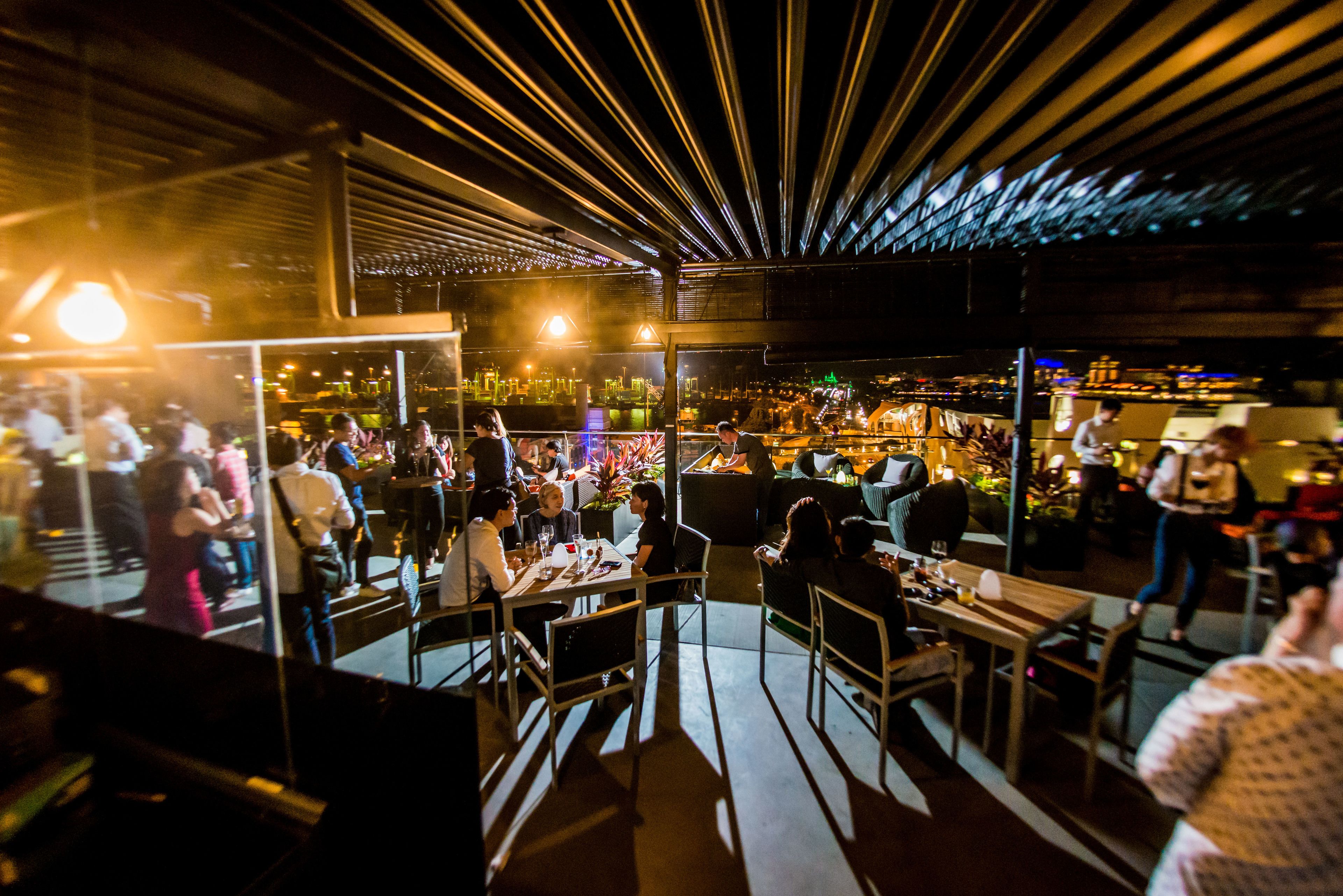 A bustling restaurant with a modern interior, featuring a mix of seating arrangements and a view of the cityscape.