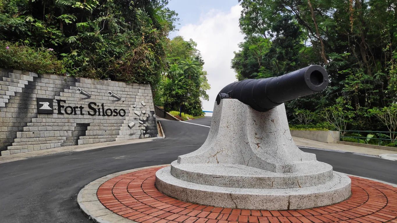 A cannon on a stone pedestal with a brick pathway and a sign reading 'Fort Siloso'.