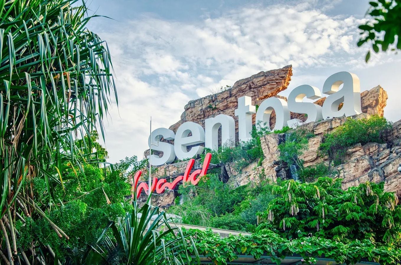 A sign with the word 'sentosa' and 'World' in large letters, set against a backdrop of greenery and a rocky cliff.