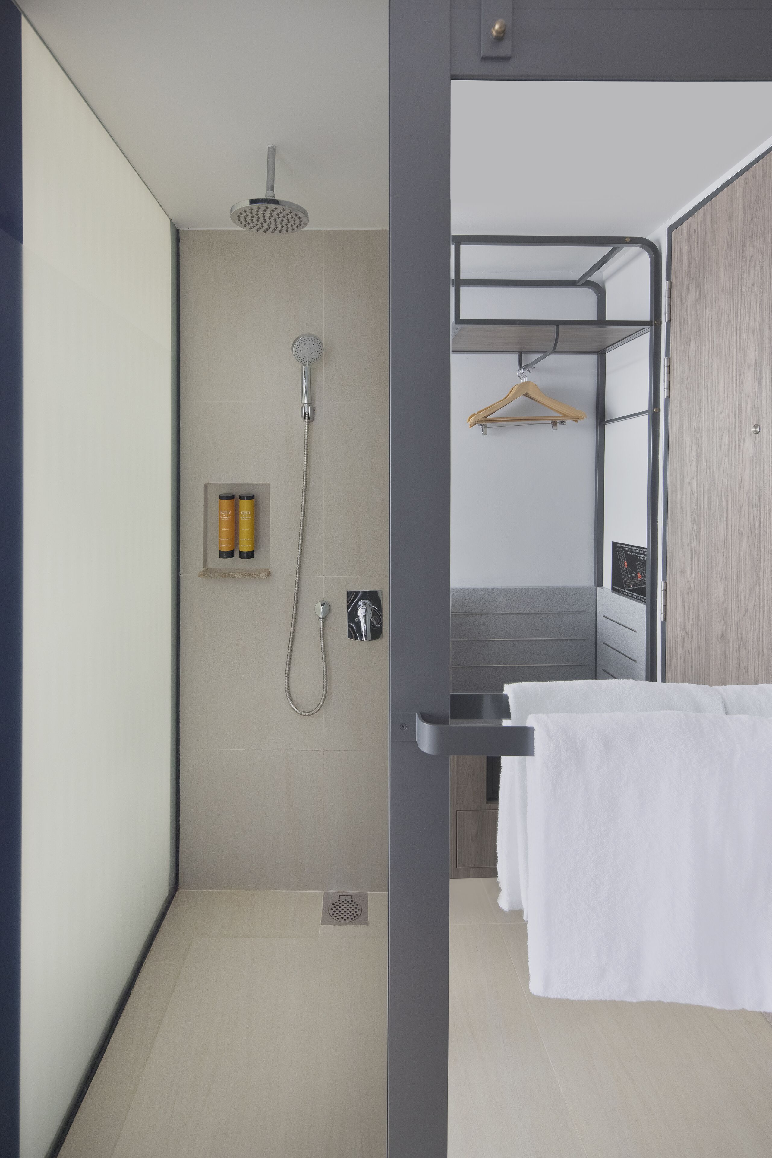 A modern bathroom with a shower, a towel rack, and a small shelf with toiletries.