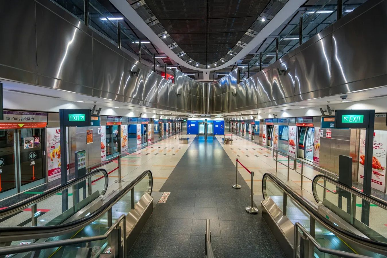 A modern train station with escalators, clear signage, and a central platform.
