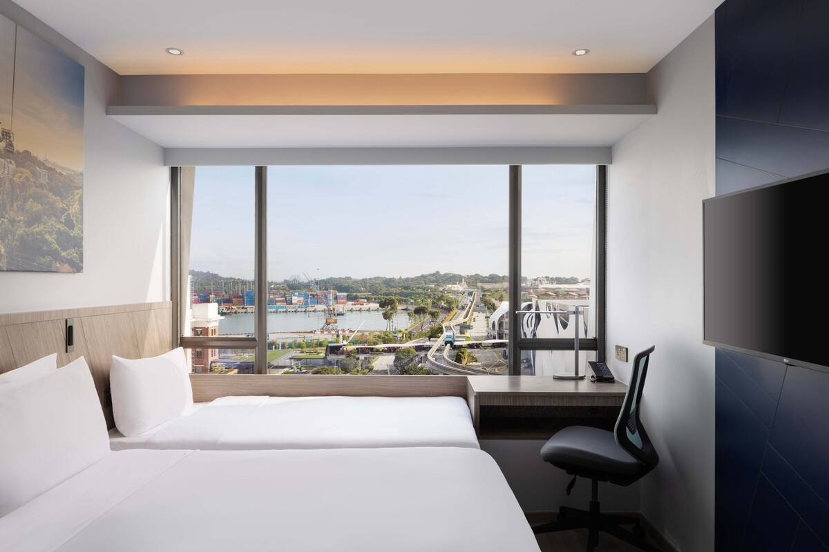 Ein modernes Hotelzimmer mit einem großen Bett, einem Schreibtisch mit Stuhl und einem Fernseher.