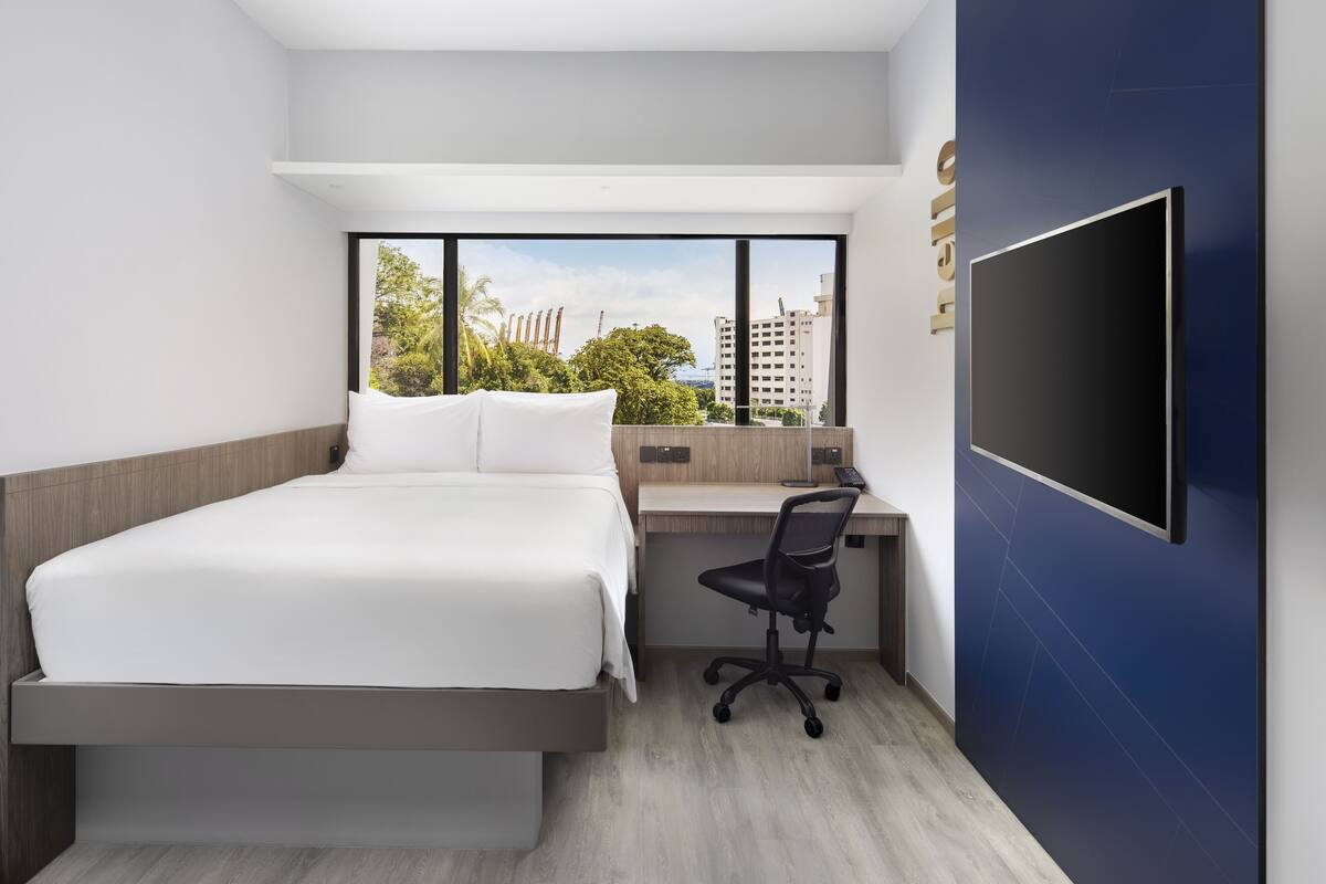 Ein modernes Hotelzimmer mit Bett, Schreibtisch und großem Fenster mit Blick auf die Stadt.
