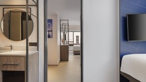 A modern hotel room with a wooden vanity, a round mirror, a flat-screen TV mounted on the wall, and a bed with a white duvet. - Travelodge Harbourfront (Singapore)