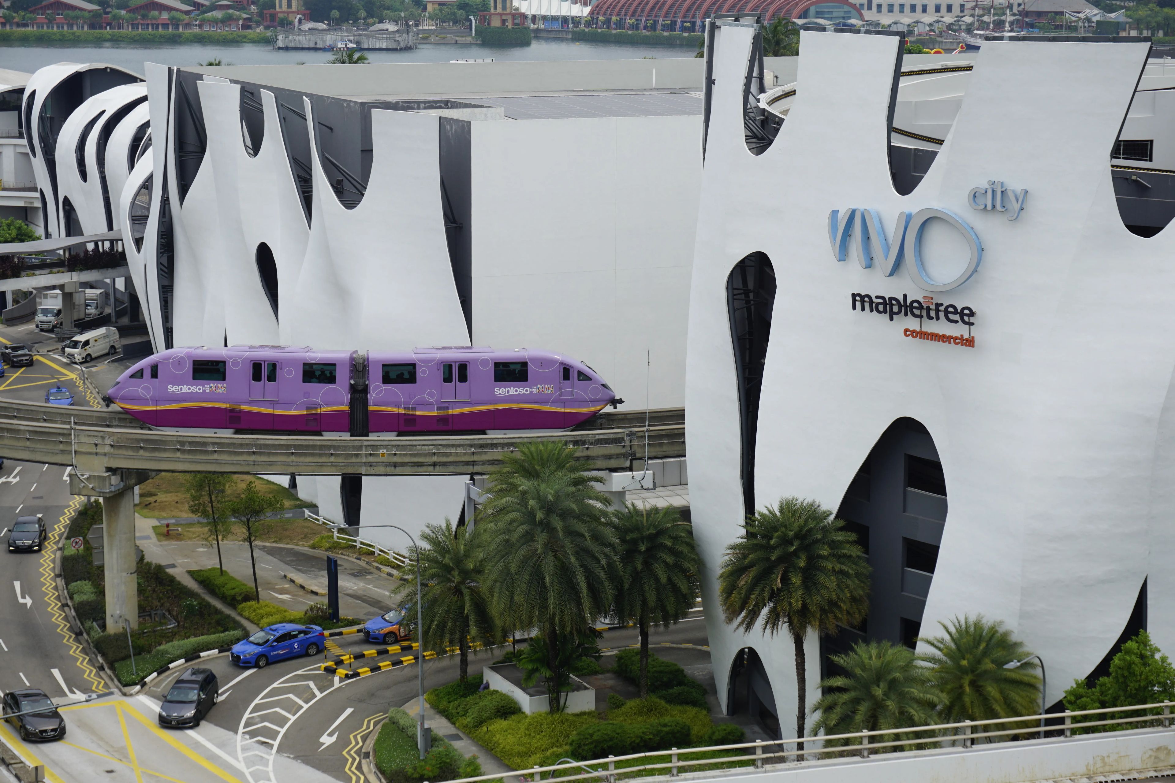 A train on an elevated track passing by a modern building with the 'WOO' logo.
