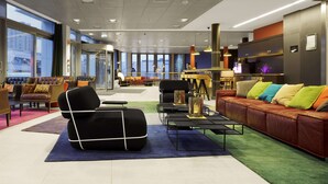 A modern lounge area with leather sofas, a black armchair, and a coffee table. There are multiple seating options and a glass partition separating the lounge from the rest of the space. - Scandic Vulkan (Oslo)