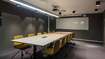 Un salón de conferencias con una larga mesa, sillas amarillas, un proyector y una pizarra.
