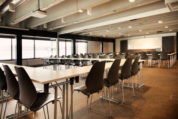 A conference room with long tables and chairs, large windows, and a projector screen. - Scandic Vulkan (Oslo)
